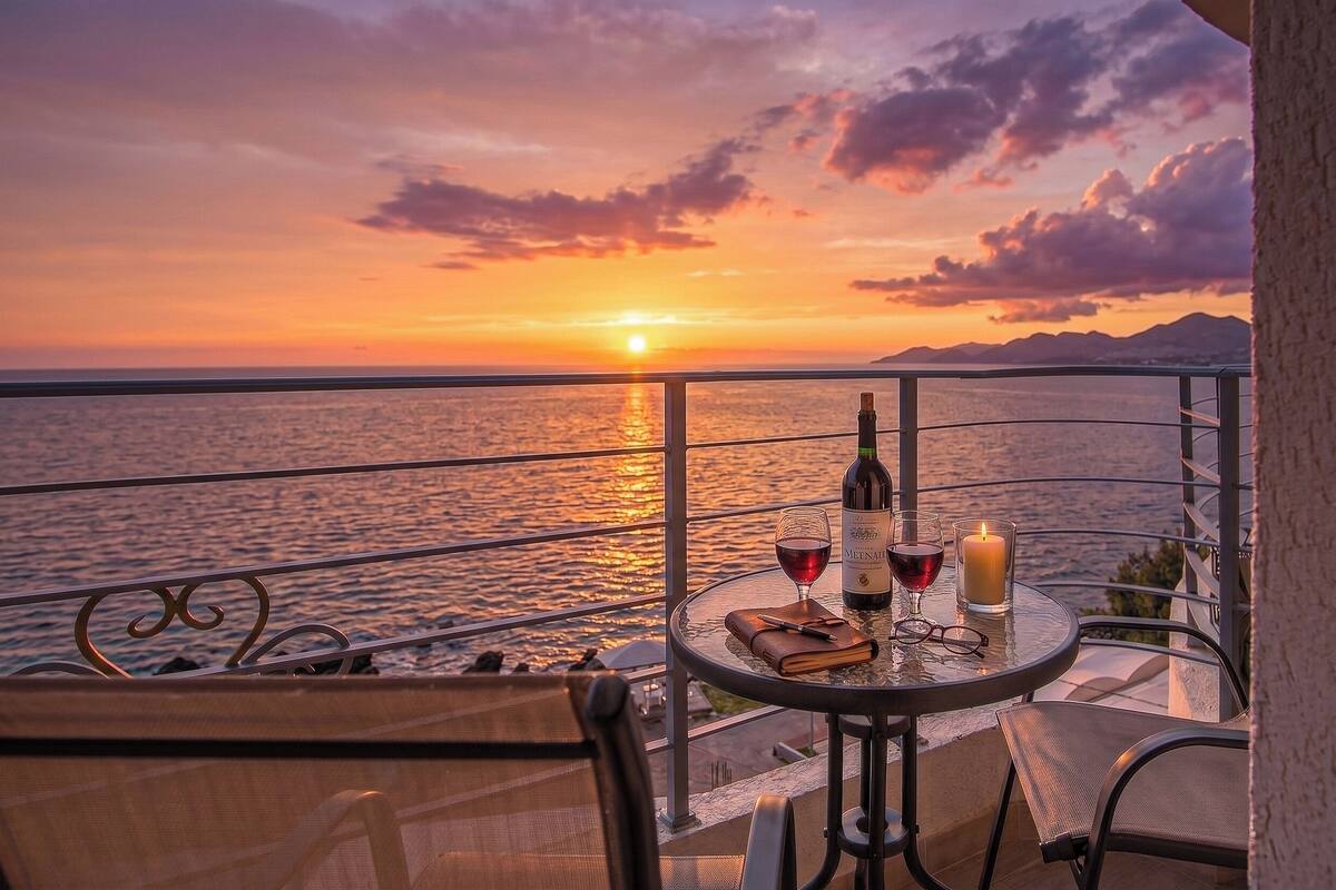 A balcony with a table set for two, a bottle of wine, a glass, and a candle.