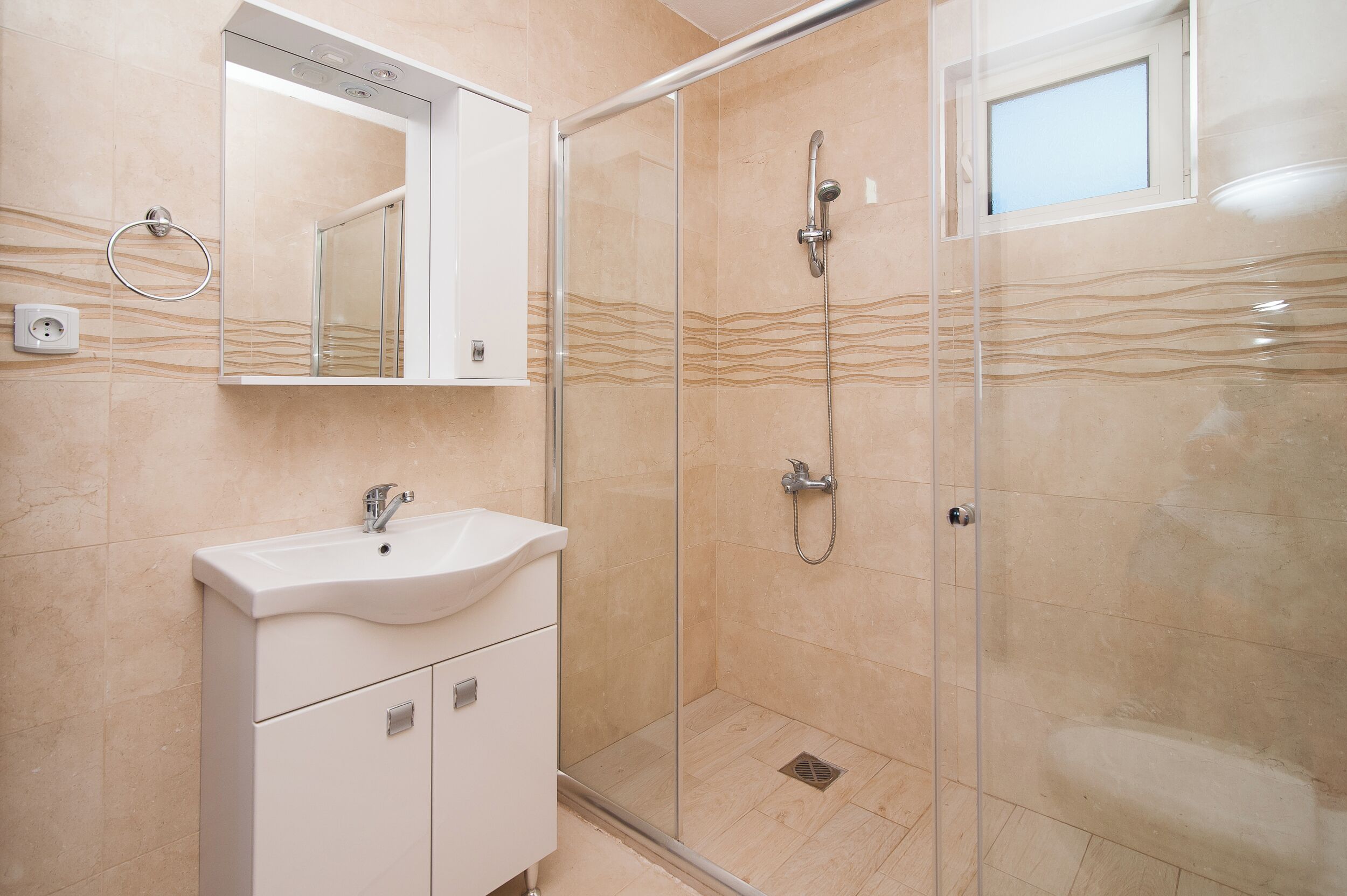 A modern bathroom with a glass-enclosed shower, a white sink, and a mirror above it.