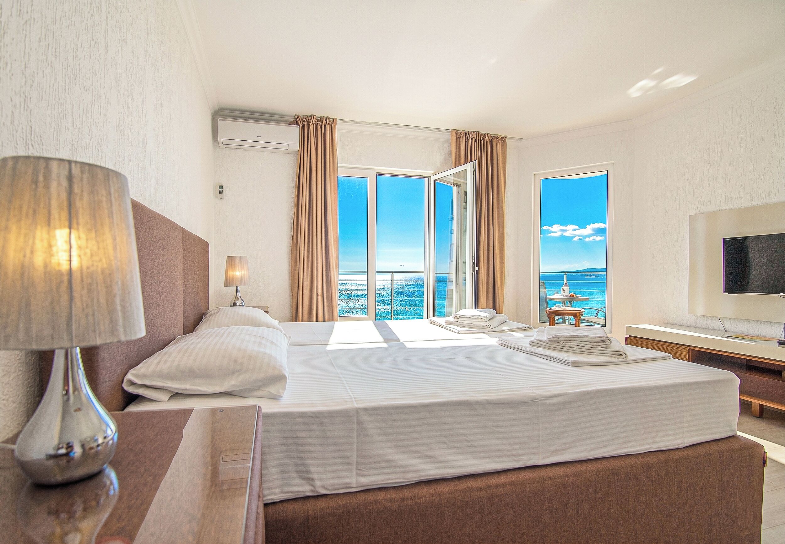 Une chambre d’hôtel avec un lit, une télévision, une lampe et une vue sur la mer.