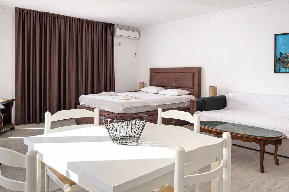 A hotel room with a bed, a white sofa, a dining table with chairs, and a painting on the wall.