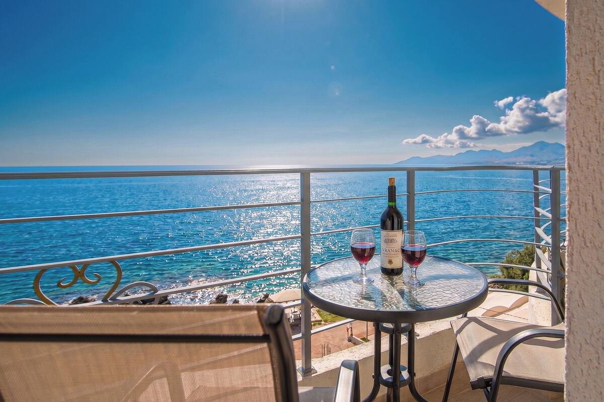 A balcony with a table, two glasses of red wine, and a bottle of wine.