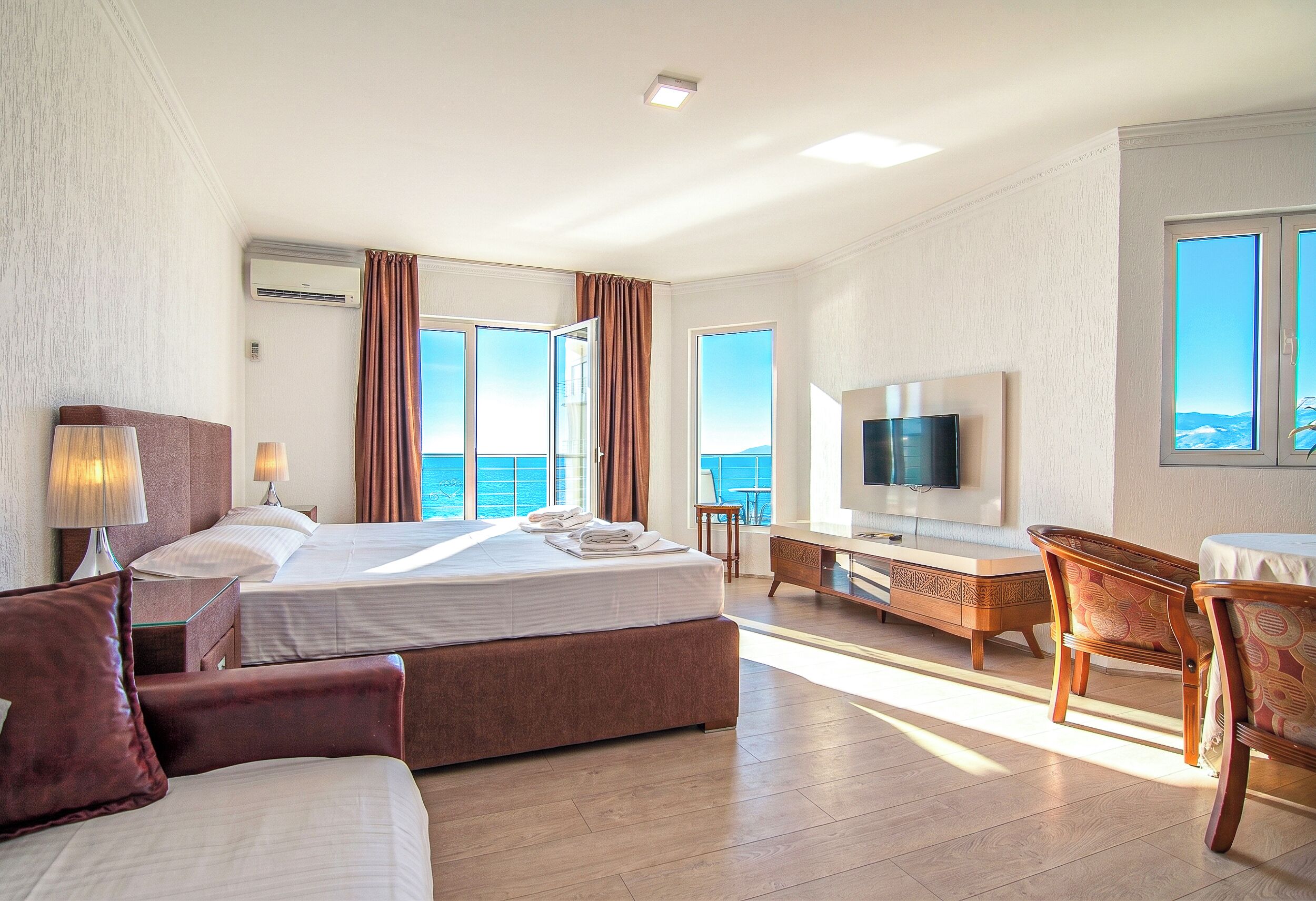 A hotel room with a bed, a TV, a desk, and a view of the sea.