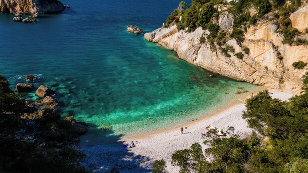 Une plage côtière aux eaux turquoise et limpides, parsemée de rochers et bordée d’un rivage sablonneux.