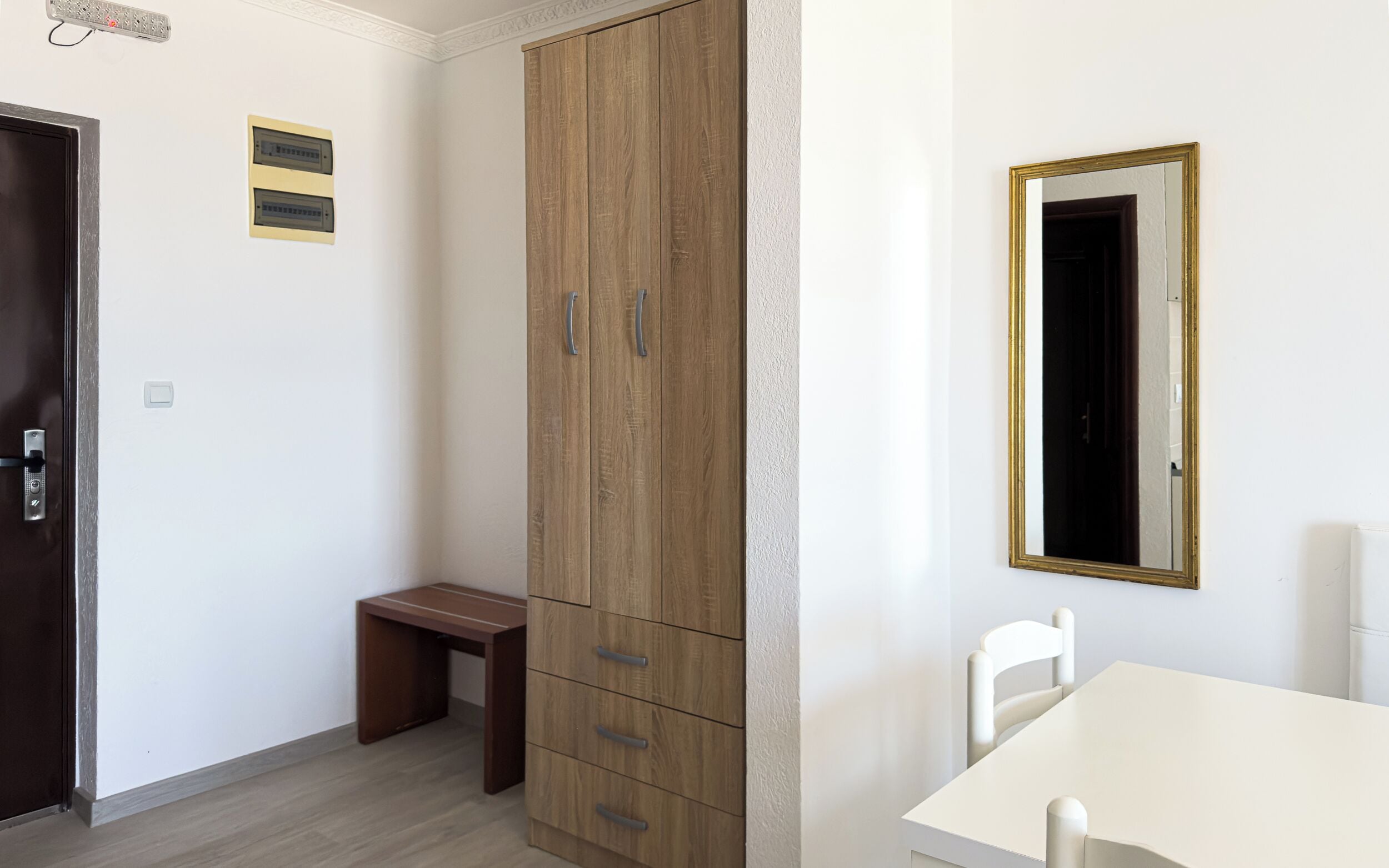 Quarto com guarda-roupa, escrivaninha, cadeira e espelho na parede.