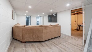 A modern living room with a large beige sectional sofa, recessed ceiling lights, and a flat-screen TV mounted on the wall. - A Home away from Home (Waterloo)