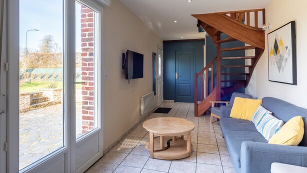 Ein geräumiges Wohnzimmer mit grauem Sofa, einem Holztisch und einer Treppe, die zu einer oberen Ebene führt.
