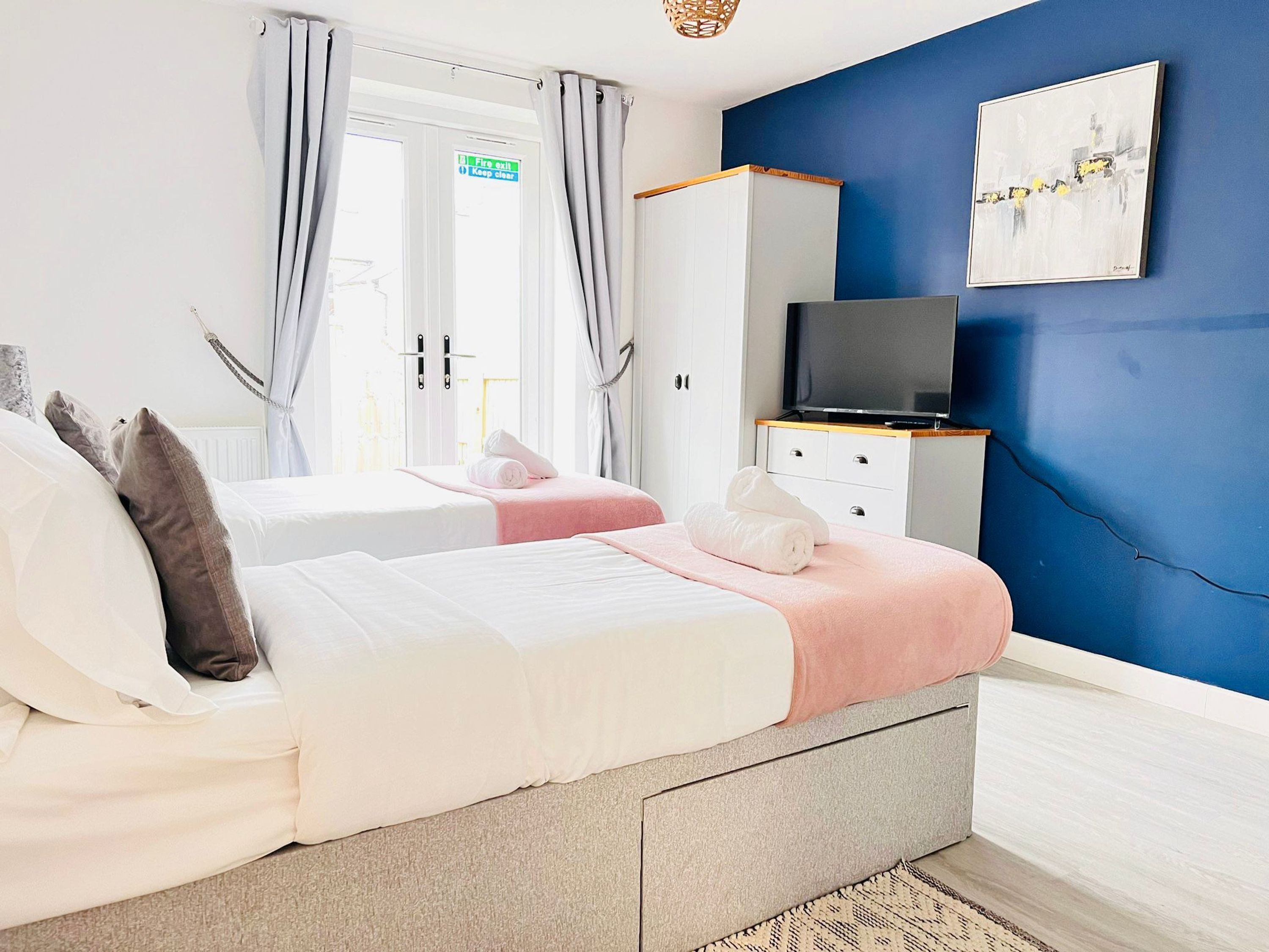Une chambre avec deux lits, une télévision, une armoire et un tableau au mur.