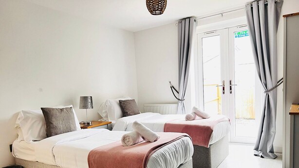 Een hotelkamer met twee bedden, een kleintje tafeltje, een lamp en uitzicht buiten via een deur.