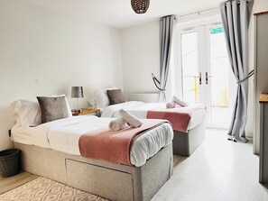 A hotel room with two beds, a small table, a lamp, and a view of the outside through a door. - Tanzanite Apartment in Cambridge (Cambridge)