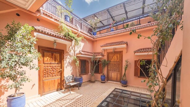 Un patio con piso de baldosas, puertas de madera, plantas en macetas y una pequeña zona de estar.