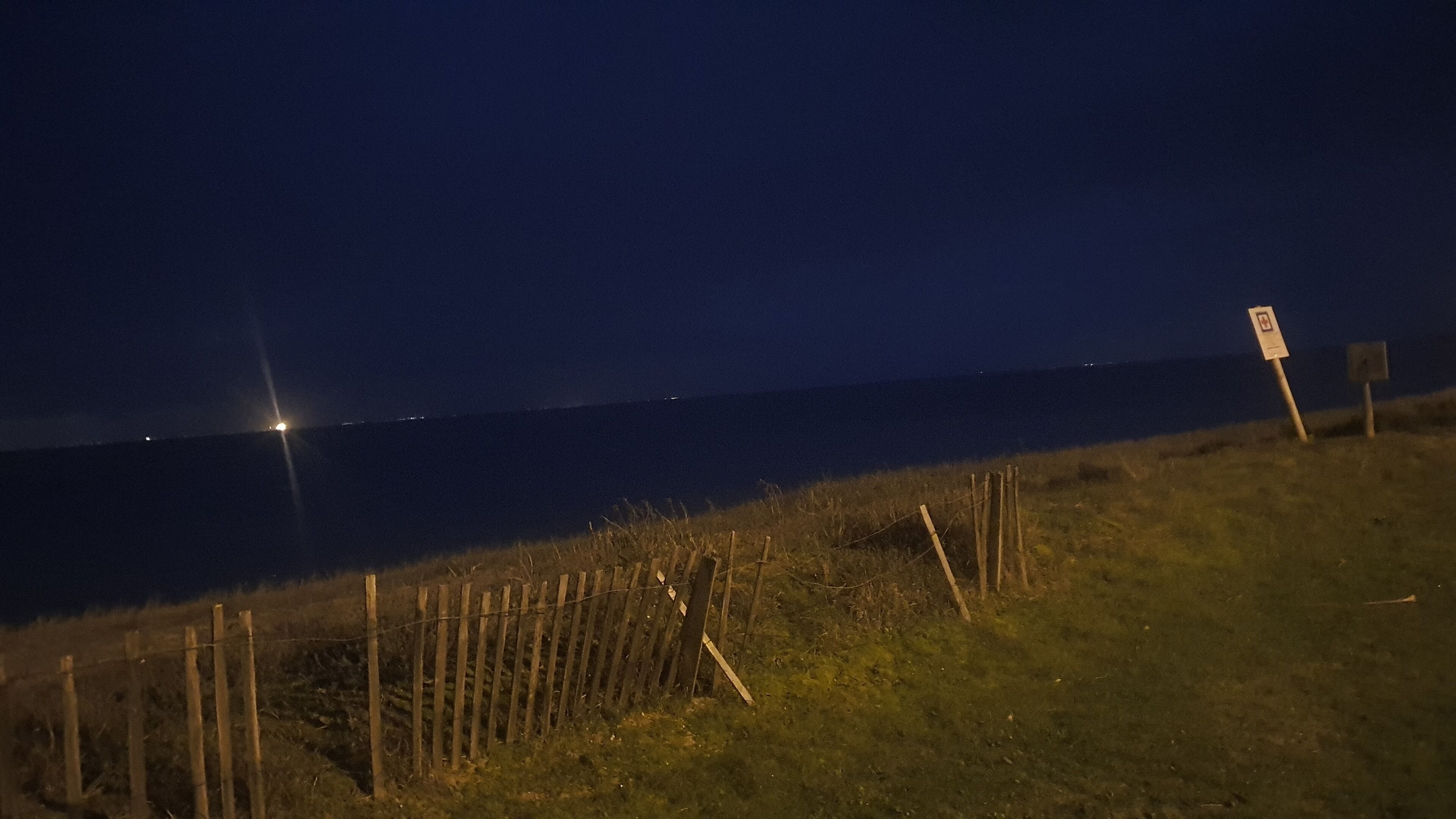 Ein Strandbild bei Nacht mit einer Holzlattenzaun und einem Wegweiser.