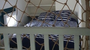 Une chambre avec un lit recouvert d’une couverture à rayures bleu marine et blanches, une tête de lit blanche et un store à voilage.