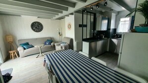 Un espace de vie compact comprenant un canapé, une petite table à manger, un coin cuisine et un lit.