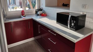 Una cocina con gabinetes rojos, encimera blanca, microondas y ventana con vistas a una zona residencial.