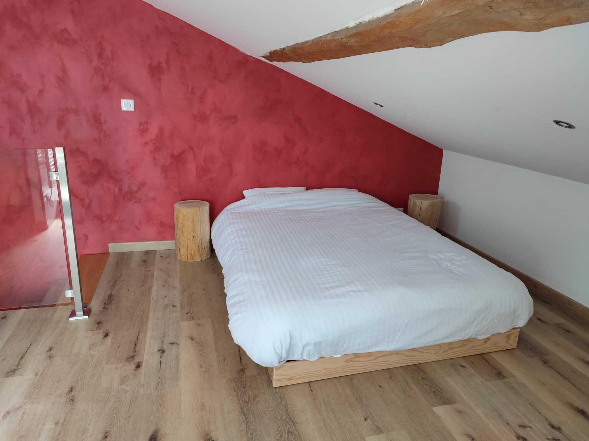 A bedroom with a wooden bed frame, a red accent wall, and a sloped ceiling.