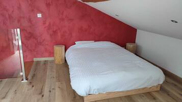 A bedroom with a wooden bed frame, a red accent wall, and a sloped ceiling.