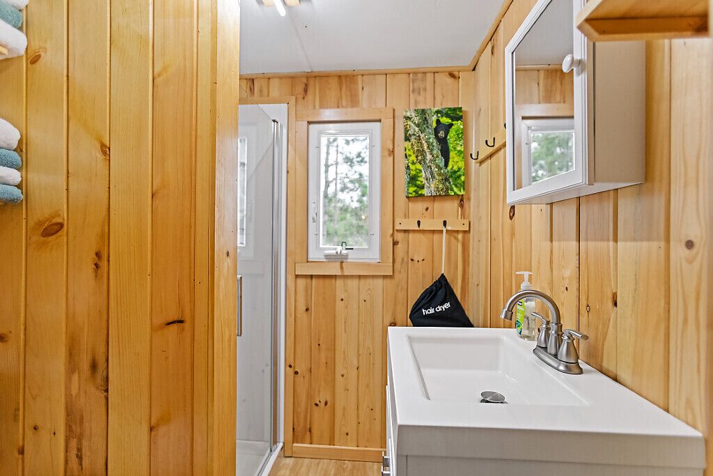 Une salle de bain aux murs lambrissés, avec un lavabo blanc, un miroir et une fenêtre.