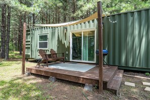 A green mobile home with a deck, two chairs, a grill, and a sliding glass door.