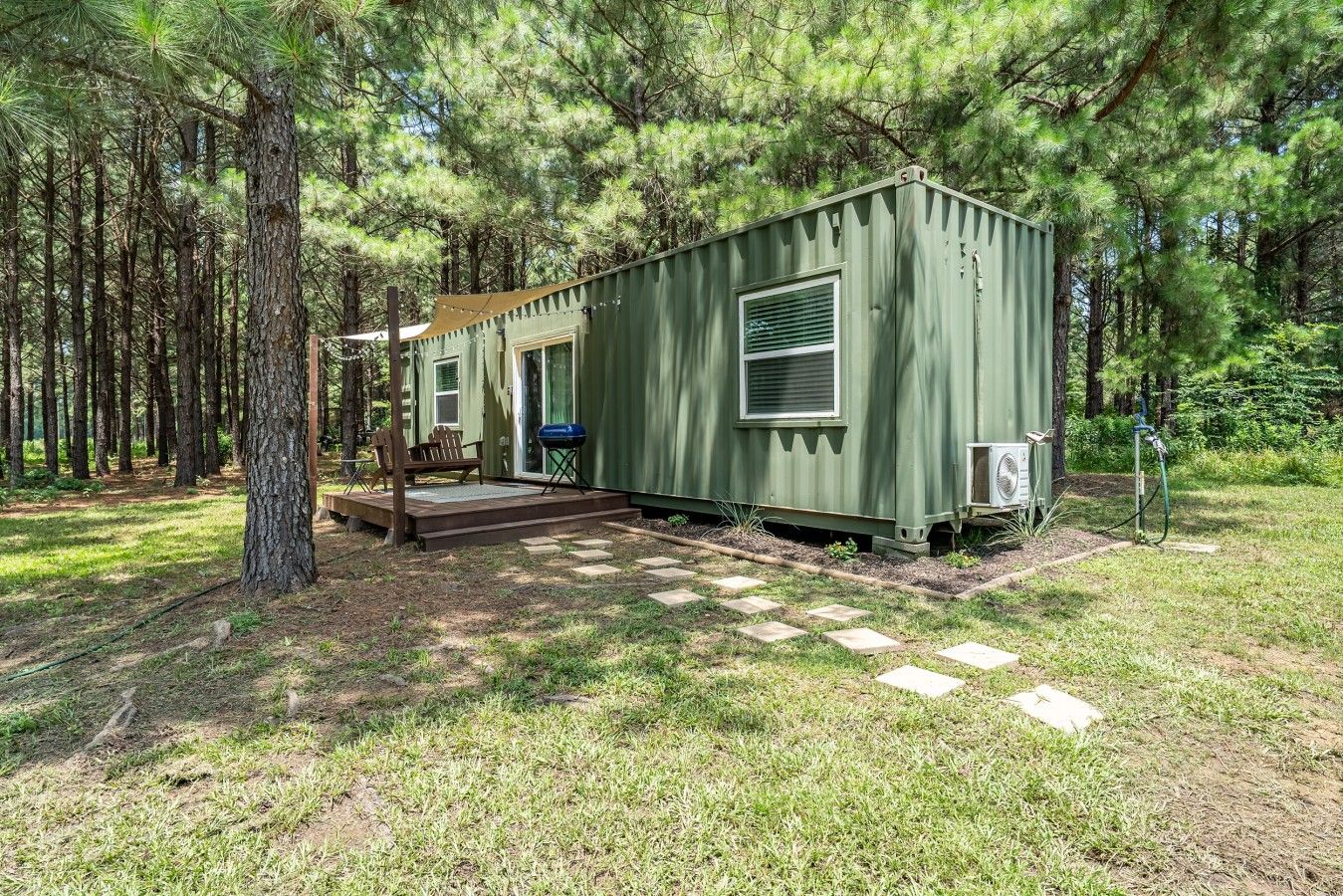 A green mobile home with a porch, a grill, and an air conditioning unit.