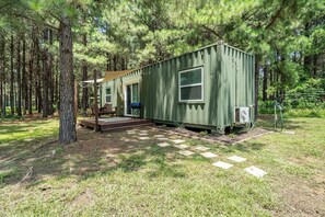A green mobile home with a porch, a grill, and an air conditioning unit.