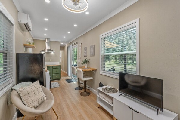 A modern living room with a flat-screen TV, a dining area, and a kitchen.