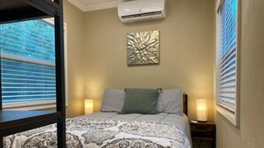 Un dormitorio con una cama, dos lámparas de noche, un aire acondicionado de pared y una ventana con persianas.