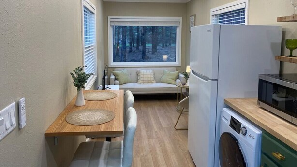 Cocina compacta con zona de comedor, lavadora y un ventanal con vistas a árboles.
