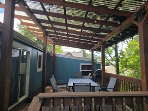 A covered outdoor patio with a table and chairs, a grill, and a view of a house in the background.