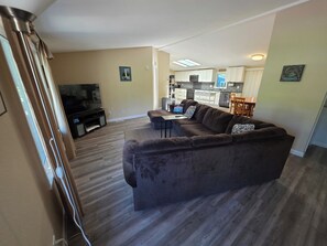 A living room with a brown sofa, a TV, and a dining area with a table and chairs.
