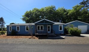 Une maison bleue de plain-pied, avec un porche à l’avant, un garage et un petit jardin devant.