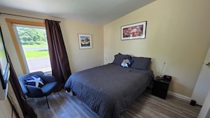 A bedroom with a bed, a chair, a nightstand, a picture on the wall, and a window with curtains. - Fisherman Friendly and minutes from the beach (Rockaway Beach)