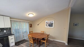 A dining area with a wooden table and chairs, a kitchen with white cabinets, and a sliding glass door. - Fisherman Friendly and minutes from the beach (Rockaway Beach)