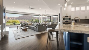 A modern kitchen with white cabinets, a granite countertop, and stainless steel appliances. There is a large window offering a view of a mountainous landscape. - Luxury 4-bedroom Retreat- stellar red rock views – St. George's Premier Getaway (Ivins)