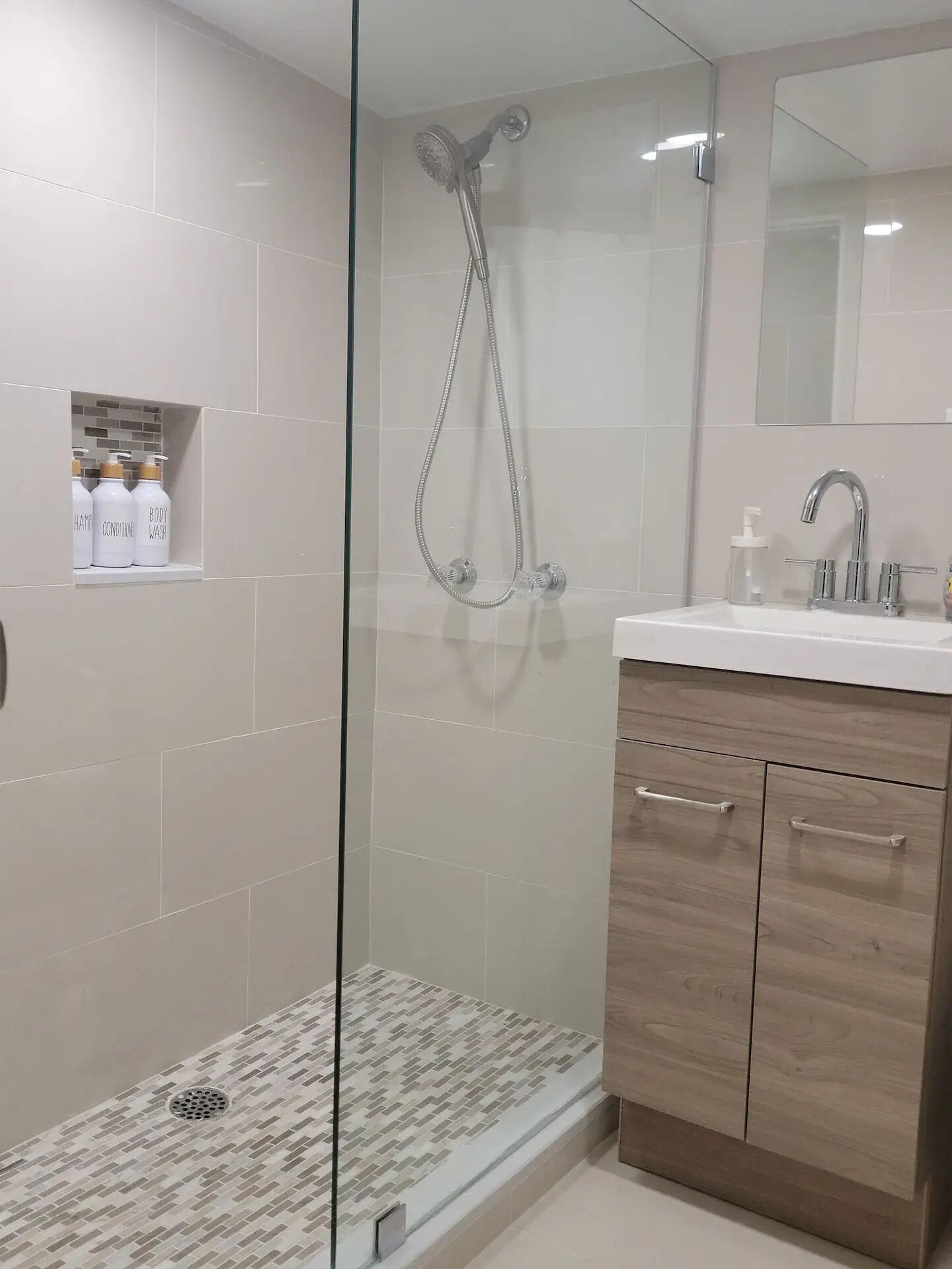 Un bany modern amb dutxa de vidre, un lavabo amb mirall i una estant amb productes de tocador.