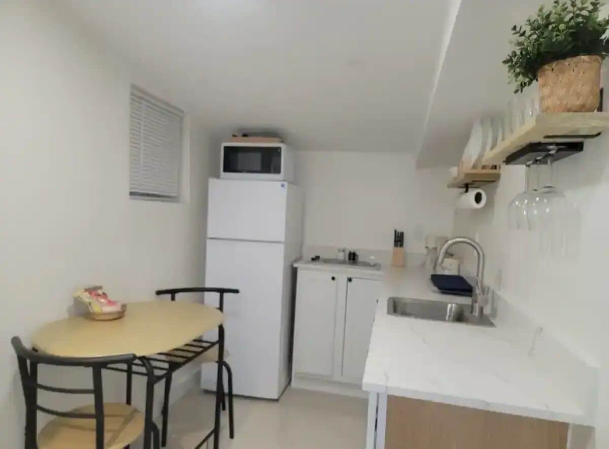 A compact kitchen with a refrigerator, a sink, and a small dining table with chairs.