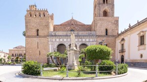 A historic building with two towers, a central archway, and a statue in the courtyard. - Angela's House (Monreale)
