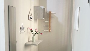 A narrow hallway with a mirror, a small shelf with a vase of flowers, a hanging bag, and a coat rack. - Angela's House (Monreale)