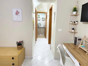 Enter a welcoming hallway leading to a kitchen area with a wooden cabinet, desk, and shelf with potted plants.