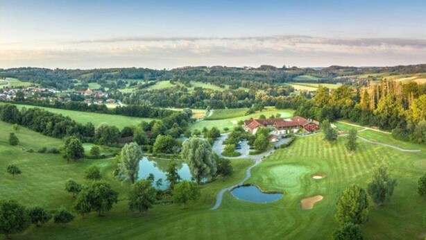 A golf course with a clubhouse, ponds, and rolling hills in the background.