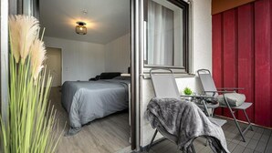 A modern bedroom with a bed, a small table with a chair, and a window with curtains.