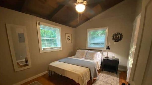 A bedroom with a bed, two windows, a ceiling fan, and a nightstand.