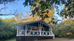 A small cabin with a porch, surrounded by trees and a gravel path.