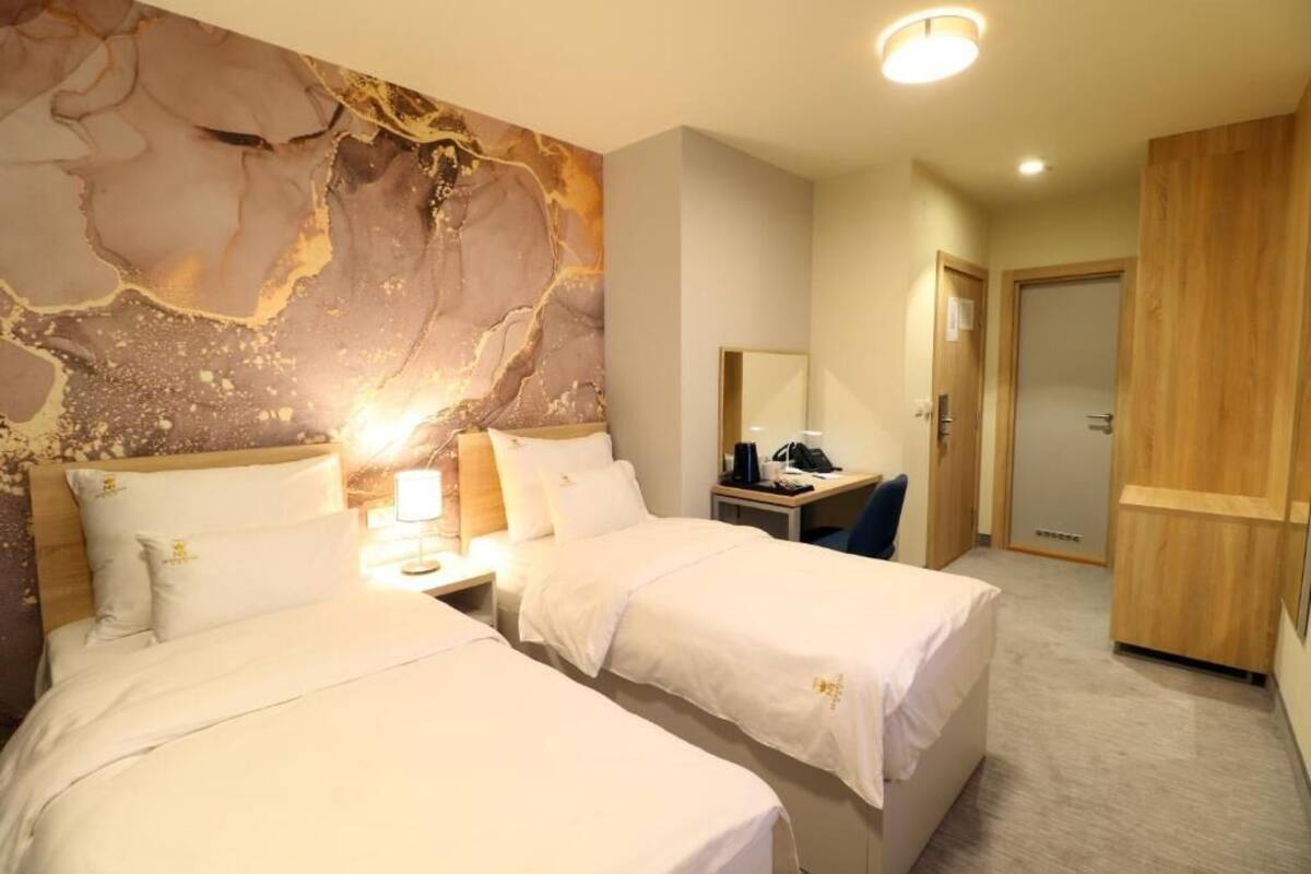 A hotel room with two beds, a marble wall, a desk with a chair, and a wooden wardrobe.