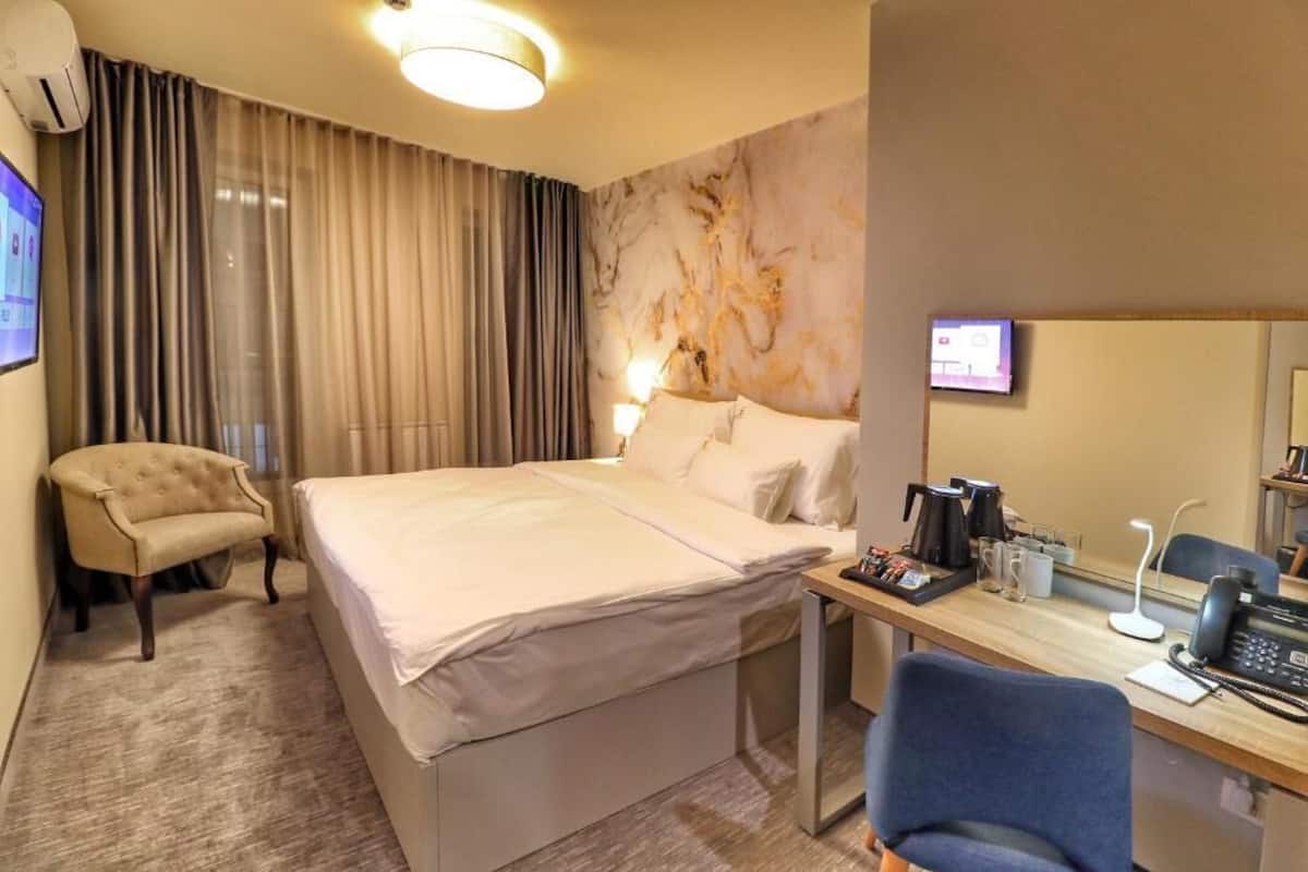 A hotel room with a bed, a desk with a phone, a chair, a coffee maker, and a TV on the wall.