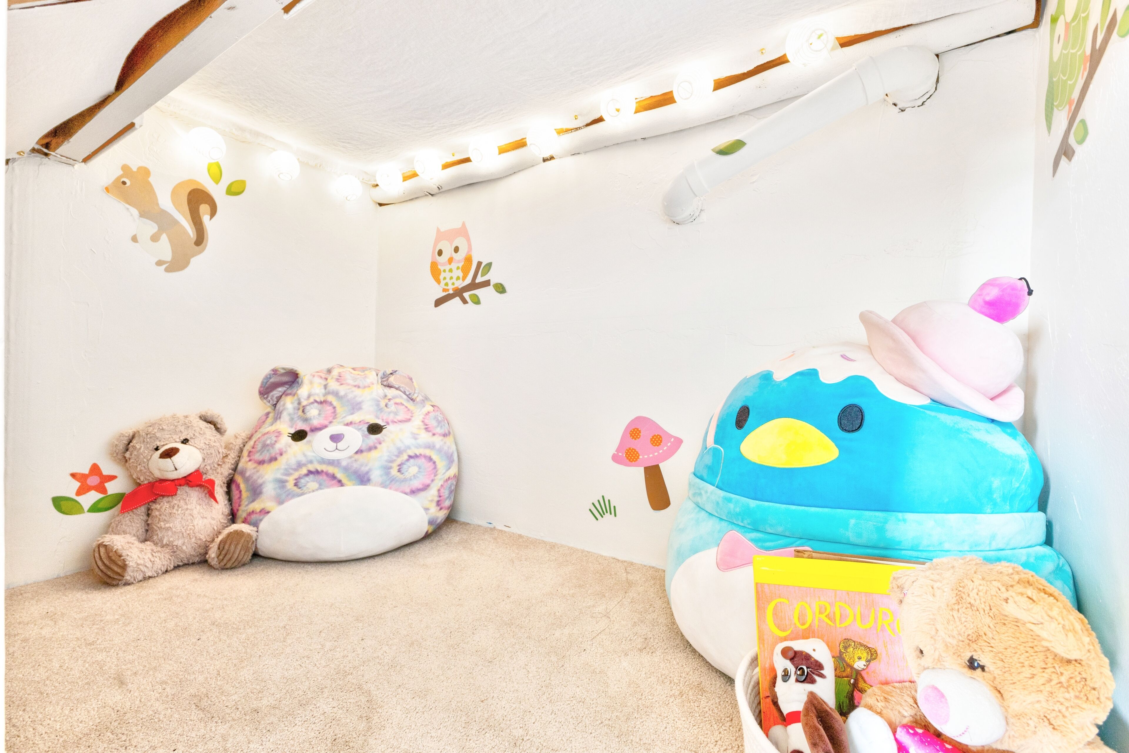 Une chambre d’enfant avec un lit, des peluches, des autocollants muraux et un luminaire au plafond.