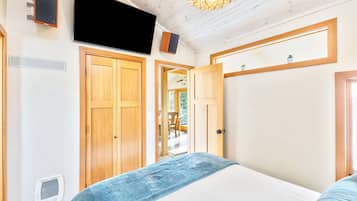 A bedroom with a bed, wooden wardrobe, a television, and a ceiling light fixture.