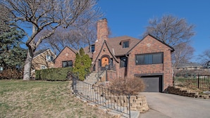 A two-story brick house with a prominent chimney, a front porch, and a garage. - Spacious Family Retreat: King Beds+Arcade+Playground. Minutes from Zoo/Downtown (Omaha)