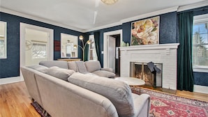 A living room with a beige sectional sofa, a fireplace, and a large window with curtains. - Spacious Family Retreat: King Beds+Arcade+Playground. Minutes from Zoo/Downtown (Omaha)