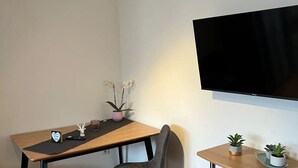 Et moderne værelse med et træspisebord, to stole, et fladskærms-tv ophængt på væggen og en lille plante på et sofabord.