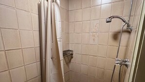 Et lille badeværelse med bruser, toilet og badekar.